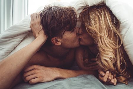Mann und Frau knutschen im Bett unter der Bettdecke