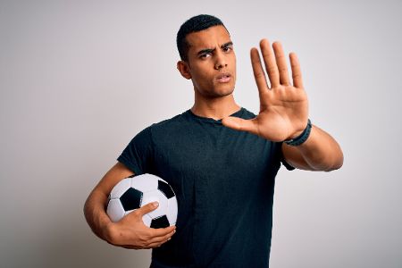 Mann mit Fußball unterm Arm hebt abwehrend eine Hand
