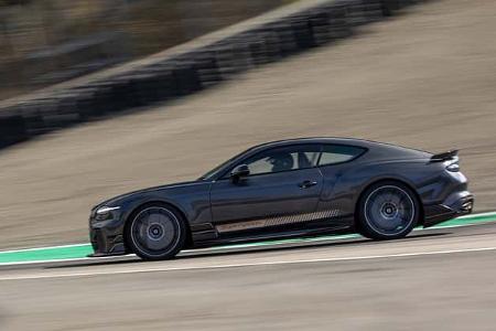 Das Foto zeigt einen Bentley Supersports in Anthrazit in Fahrt auf einer Rennstrecke. Das Sportcoupé ist in dynamischer Seitenansicht mit aerodynamischen Anbauteilen, markanten Leichtmetallrädern und festem Heckspoiler zu sehen. Die Mitzieheraufnahme betont die Geschwindigkeit auf der Strecke.