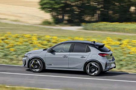 Das Bild zeigt einen Opel-Kompaktwagen als fünftüriges Schrägheck in Seitenansicht auf einer Landstraße. Auffällig sind die zweifarbige Lackierung mit schwarzem Dach, sportliche Leichtmetallräder, Dachspoiler und der seitliche „GSe“-Schriftzug. Die Szene ist als Mitzieher fotografiert, im Hintergrund liegen Felder und ein Sonnenblumenstreifen.