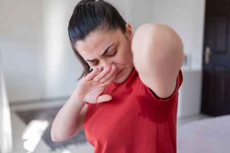 Junge Frau betrachtet Schweißfleck unter ihrem Arm und hält sich die Nase zu