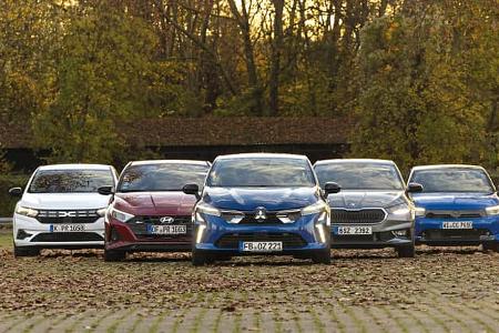 Fünf Kleinwagen-Modelle (Mitsubishi Colt, Dacia Sandero, Opel Corsa, Skoda Fabia, Hyundai i20) nebeneinander auf einem Parkplatz in herbstlicher Umgebung, frontal fotografiert.