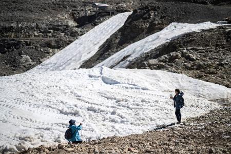 Touristen fotografieren in den Schweizer Alpen Schneereste an einer Skipiste. 