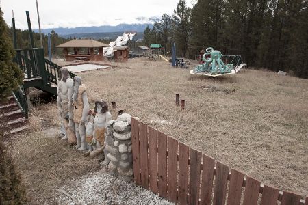 Blick auf das Gelände eines verlassenen Freizeitparks mit Kinderkarussell und Teppichrutsche im Hintergrund