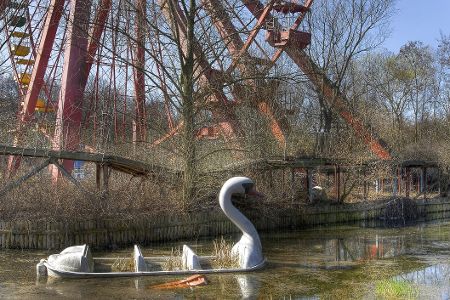 Halb versunkenes, überwachsenes Schwanenboot vor einem Riesenrad