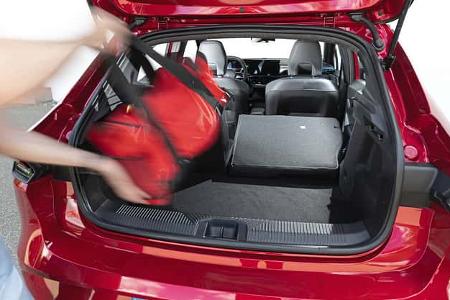 Der geöffnete Kofferraum eines Renault Clio Full Hybrid E-Tech 160, eine Person lädt eine rote Tasche ein. Die Rücksitze sind teilweise umgeklappt, der Blick geht durch den Innenraum nach vorne.