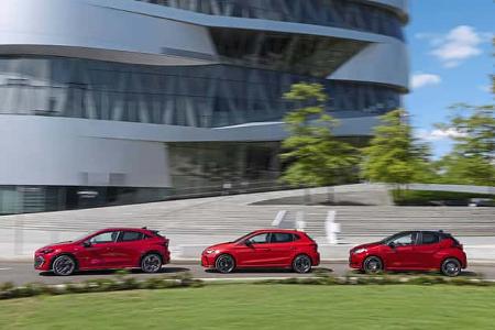 Drei rote Kompaktwagen (Renault Clio Full Hybrid E-Tech 160, Toyota Yaris Hybrid, Seat Ibiza TSI) fahren nebeneinander vor einem modernen Gebäude.