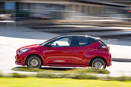 Toyota Yaris Hybrid fährt in der Stadt, Seitenansicht, rote Lackierung, moderner Kleinwagen, Bewegungseffekt.