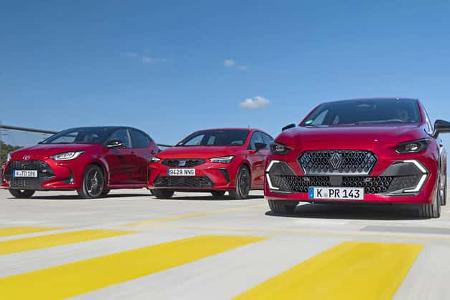 Drei rote Kompaktwagen (Renault Clio, Seat Ibiza, Toyota Yaris Hybrid) nebeneinander auf einer Fahrbahn, Frontansicht.