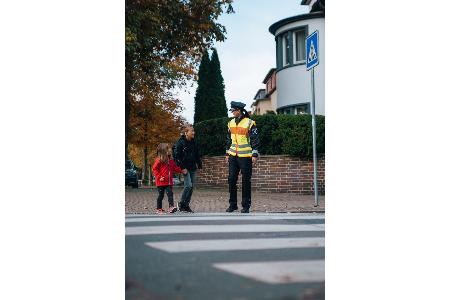 Polizistin führt Kinder über einen Zebrastreifen