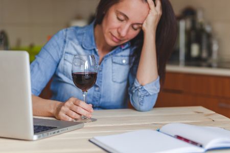 Gestresste Frau sitzt mit Glas Rotwein vor dem Laptop