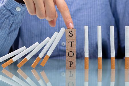 Person tippt auf aufgestapelte Würfel, auf denen das Wort Stop steht, die zwischen Zigaretten aufgestellt sind