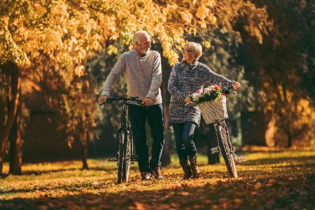Älteres Ehepaar schiebt Fahrräder durch einen herbstlichen Park