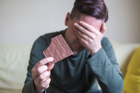 Gestresster Mann hält angebissene Tafel Schokolade in der Hand