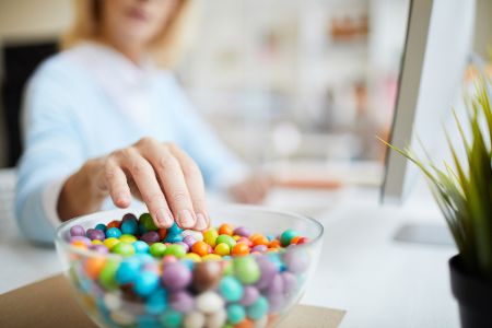 Frau am Laptop greift in Schüssel mit M&Ms