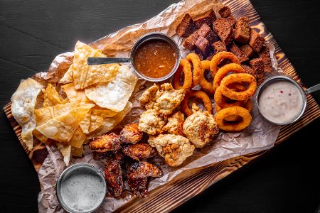 Tablett mit allerhand frittierten Speisen, darunter Tacos, Chicken Wings und Zwiebelringe