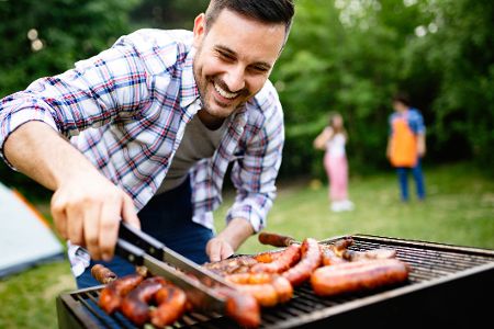 Mann grillt Würstchen im Park