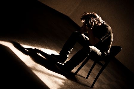 Junger Mann sitzt verzweifelt auf einem Stuhl im leeren Raum
