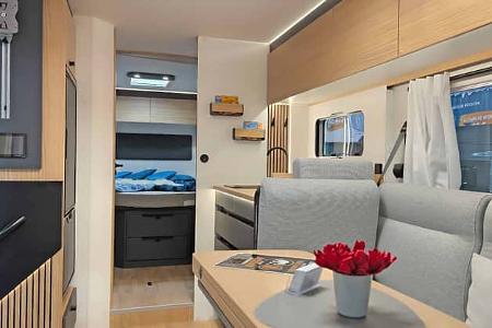 Modern gestalteter Innenraum eines vollintegrierten Mooveo Reisemobils (Modell INT-78 QBF Al-Ko): Blick von der Sitzgruppe durch den Durchgang ins Heck mit Queensbett und Stauraum.