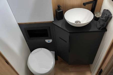 Kompaktes WC mit Waschbecken und Waschtisch im Sanitärbereich des Mooveo INT-78 QBF Al-Ko. Praktische Ablageflächen und moderne Armaturen.