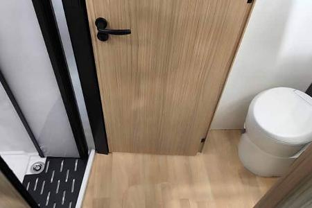 Raumbad mit Dusche, Waschbecken und WC im Mooveo INT-78 QBF Al-Ko. Moderne Fliesenoptik und helle Beleuchtung schaffen ein angenehmes Ambiente.