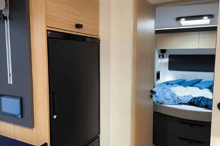 Kühlschrank im Küchenbereich des Mooveo INT-78 QBF Al-Ko, integriert neben dem Bett. Moderne Front und praktische Griffmulden.