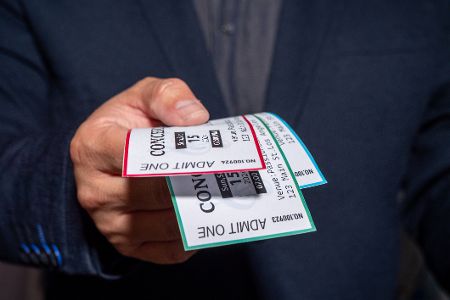 Mann streckt einem drei Konzerttickets entgegen