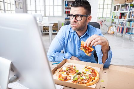 Mann isst alleine eine Pizza vor seinem Laptop im Büro