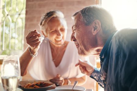 Älteres Paar lacht beim Kochen und Probieren des Essens