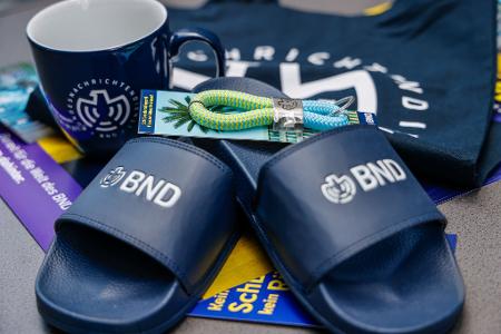 Im Merchandise-Shop gibt es T-Shirts und auch Badelatschen mit BND-Logo. 