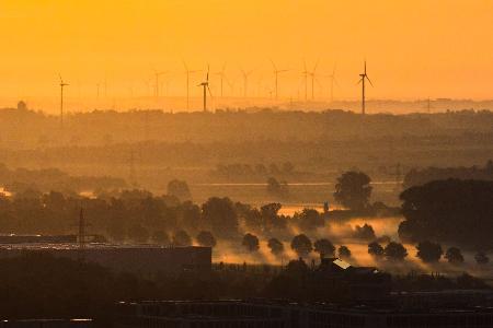 Windräder und Nebel zeichnen sich im Licht der aufgehenden Sonne in der Region Hannover ab.