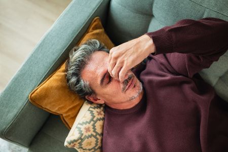 Mann liegt auf dem Sofa und hält sich erschöpft den Kopf