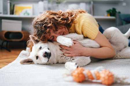 Frau kuschelt mit ihrem Hund auf dem Teppich