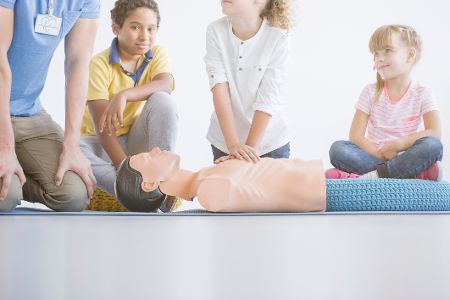 Mädchen übt vor der Klasse Herzdruckmassage an einer Puppe