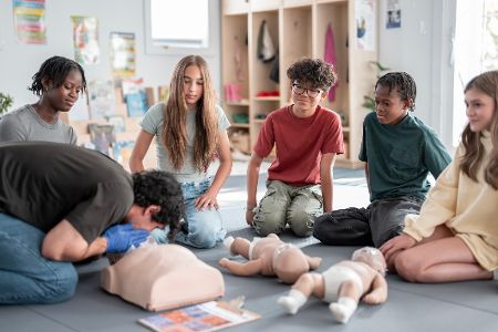 Kinder schauen bei einer Herzdruckmassage mit Mund-zu-Mund-Beatmung an einer Puppe zu