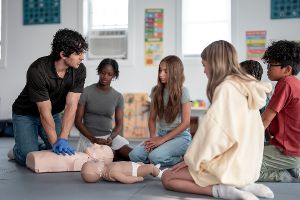 Lehrer zeigt Kindern eine Reanimation an einer Puppe