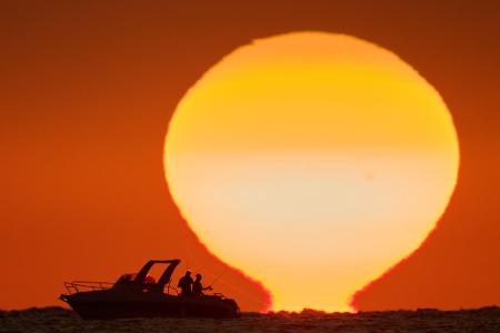 Fischer zeichnen sich als Silhouetten auf einem Boot ab, während die Sonne im Libanon über dem Mittelmeer untergeht.