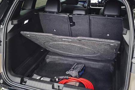 Das Foto zeigt den Kofferraum des Jeep Compass Elektro. Die hochgeklappte Ladebodenplatte gibt ein Unterbodenfach frei, in dem ein Ladekabel und weiteres Ladezubehör verstaut sind; die umklappbaren Rücksitzlehnen und der Blick nach vorn ins Cockpit sind sichtbar.
