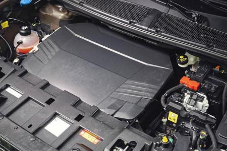 Die Aufnahme zeigt den Motorraum eines Jeep Compass Elektro, wie im Dateinamen angegeben. Unter der großflächigen Motorabdeckung sind Komponenten des elektrischen Antriebsstrangs erkennbar, darunter Hochvolt-Baugruppen mit Warnsymbolen, Kühlmittel-Ausgleichsbehälter und Verkabelung. Es handelt sich um eine Detailansicht des vorderen Aggregatraums.