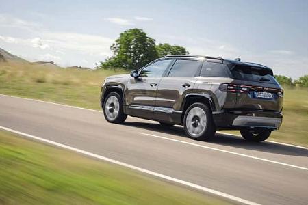 Das Bild zeigt einen Jeep Compass Elektro in Fahrt auf einer Landstraße. Der kompakte Elektro-SUV ist aus schräger Heck‑Seitenansicht zu sehen, mit markanten LED-Rückleuchten und fünf Türen. Die Aufnahme vermittelt Fahrdynamik in ländlicher Umgebung.