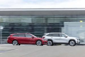 Das Fahrbild zeigt einen Skoda Kodiak und einen Skoda Superb in Seitenansicht. Der silberne SUV und der rote Kombi fahren parallel vor einer verglasten Gebäudefassade, die Bewegungsunschärfe betont die Fahrt. Die Aufnahme wirkt urban und steht im Kontext einer Kaufberatung.