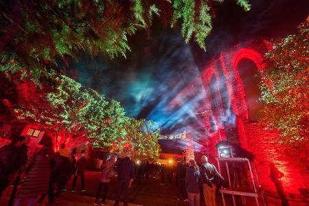 Besucher des Lichtkunstfestival Rheinleuchten wandeln durch den illuminierten Klostergarten in Oberwesel. 