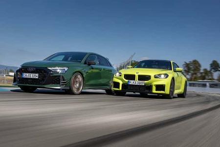 Die Fahraufnahme zeigt einen Audi RS3 Competition Limited und einen BMW M2 Coupe auf dem Hockenheimring. Beide Kompaktsportler sind in einer schnellen Rechtskurve aus Frontperspektive zu sehen, mit betonten Lufteinlässen, breiten Reifen und dynamischer Bewegungsunschärfe. Reifenspuren und Streckenbegrenzungen unterstreichen den Track-Kontext.
