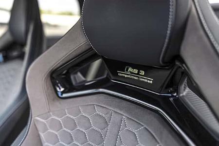 Die Detailaufnahme zeigt den Innenraum eines Audi RS3 Competition Limited, erkennbar am in die Sitzschale integrierten „RS 3 competition limited“-Schriftzug. Abgebildet ist ein Sportsitz/Schalensitz mit Wabensteppung, kontrastierenden Ziernähten und integrierter Kopfstütze; die hochglänzende Sitzschale mit Öffnungen betont den Leichtbaucharakter.