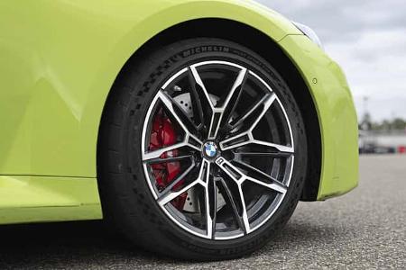 Detailaufnahme des Vorderrads eines BMW M2 Coupe. Sichtbar sind eine mehrspeichige Leichtmetallfelge mit BMW-Emblem, rote Bremssättel und eine gelochte Bremsscheibe sowie ein Hochleistungsreifen mit Michelin‑Pilot‑Sport‑Cup‑Beschriftung. Die Aufnahme zeigt das Fahrzeug im Stand auf Asphalt.