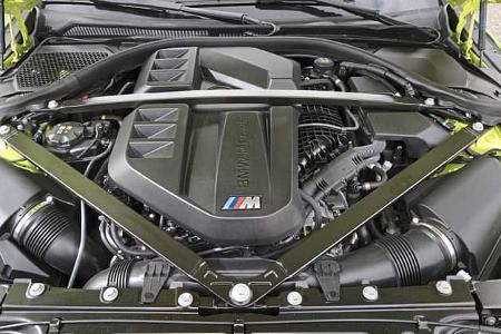 Die Aufnahme zeigt den Motorraum eines BMW M2 Coupe mit geöffneter Haube. Zentral liegt der von einer „BMW M Power“-Abdeckung verdeckte Antrieb, flankiert von beidseitigen Luftfiltergehäusen und Ansaugtrakten; eine quer verlaufende Domstrebe stabilisiert die Frontstruktur. Die frontal aufgenommene Detailansicht macht Leitungen, Verschlauchung und Kunststoffabdeckungen deutlich erkennbar.