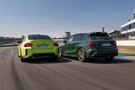 Das Foto zeigt einen Audi RS3 Competition Limited und einen BMW M2 Coupe auf dem Hockenheimring, aufgenommen aus der Heckperspektive bei schneller Kurvenfahrt. Beide Fahrzeuge sind als Kompaktsportler mit breiten Diffusoren und mehrflutigen Abgasanlagen zu sehen, was die Track-Orientierung der Szene unterstreicht. Die Bewegungsunschärfe und die Curbs der Rennstrecke verdeutlichen den dynamischen Einsatz auf dem Kurs.