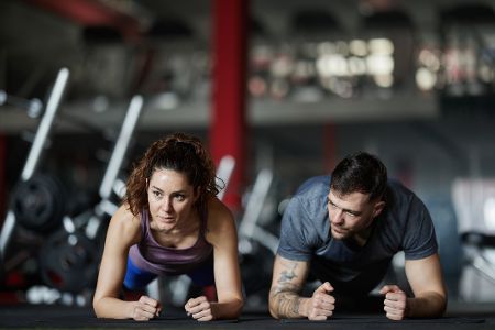 Mann macht sehr dicht neben einer Frau Fitnessübungen am Boden
