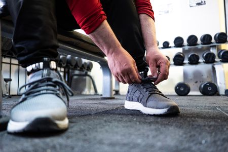 Mann im Fitnessstudio schnürt sich die Schuhe zu