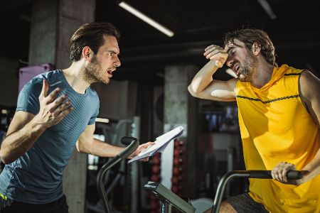 Trainer mit Klemmbrett regt sich über erschöpften Sportler auf